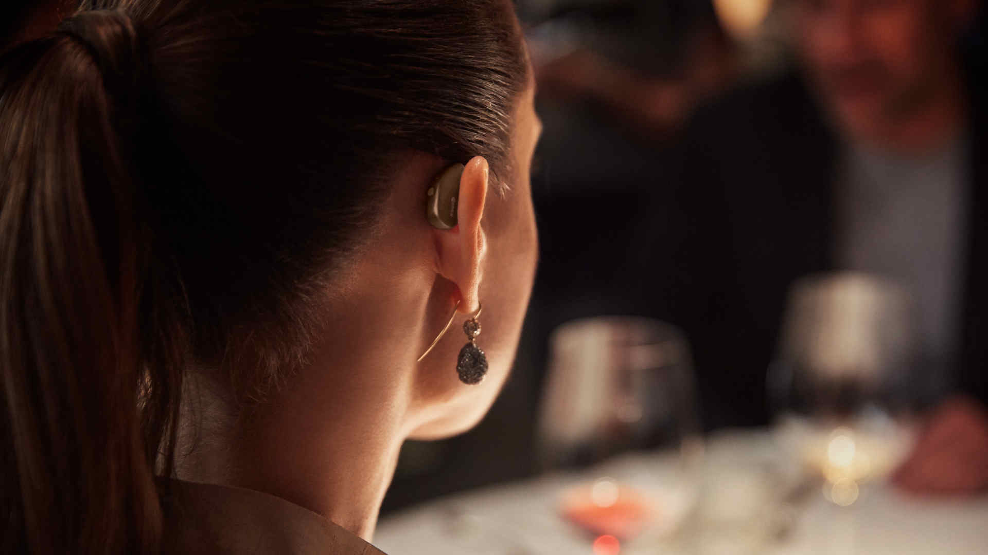 A woman in a candle-lit restaurant wearing a Widex Moment hearing aid
